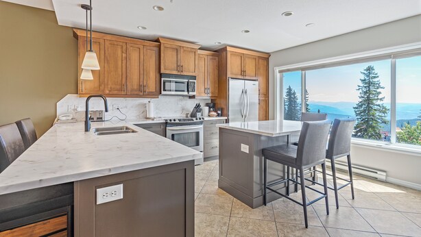 A modern kitchen with wooden cabinets, a large island, and a view of mountains. - Ultimate Slopeside Retreat – Sleeps 24 Across Two Spacious Townhomes (Silver Star Mountain)