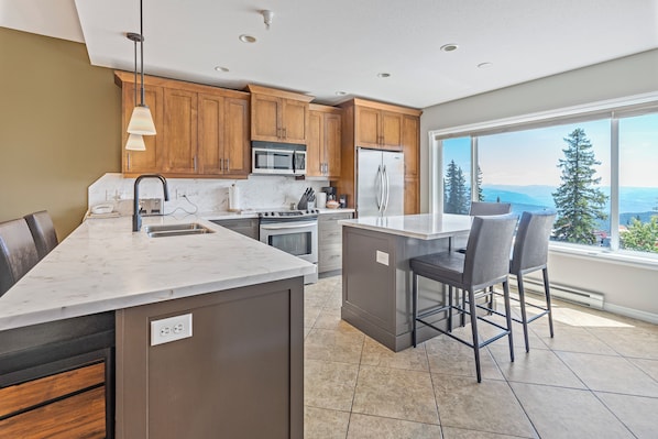 A modern kitchen with wooden cabinets, a large island, and a view of mountains.