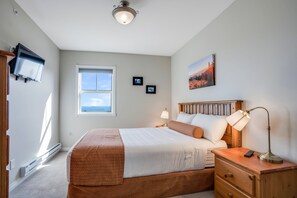 A bedroom with a bed, bedside lamp, nightstand, and a painting on the wall.