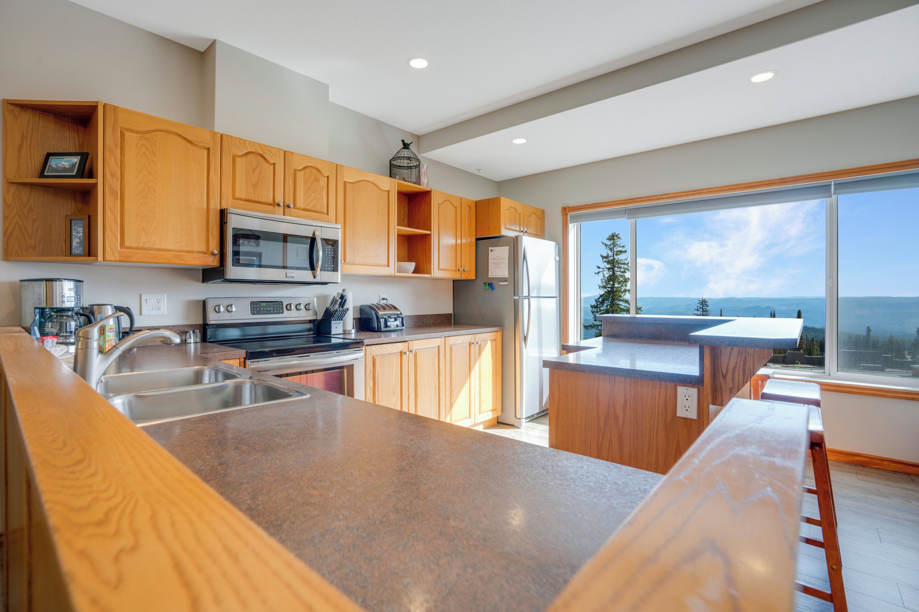 A modern kitchen with wooden cabinets, stainless steel appliances, and a large window offering a view of the ocean.
