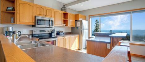 A modern kitchen with wooden cabinets, stainless steel appliances, and a large window offering a view of the ocean.