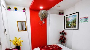 Ein kleines Hotelzimmer mit einem Einzelbett, einem Schreibtisch, einem Spiegel und einer Wand in Rot.