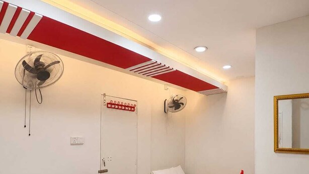 Ein Hotelzimmer mit zwei Betten, einer rot-weiß gestreiften Decke, einem Wandventilator, einem Spiegel und einem kleinen Tisch mit einem Blumenstrauß.