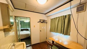 Una habitación pequeña con un lavabo, una silla de madera, una cama con cortina y un espejo.