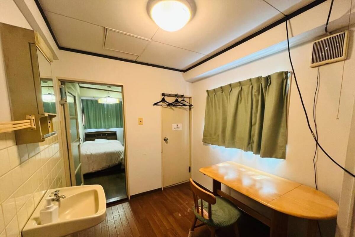 A small room with a sink, a wooden chair, a bed with a curtain, and a mirror.