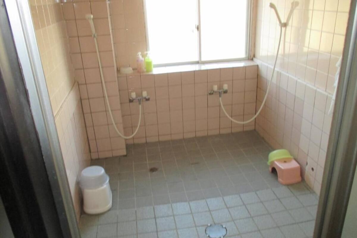 A bathroom with a window, two showerheads, a toilet, and a small stool.