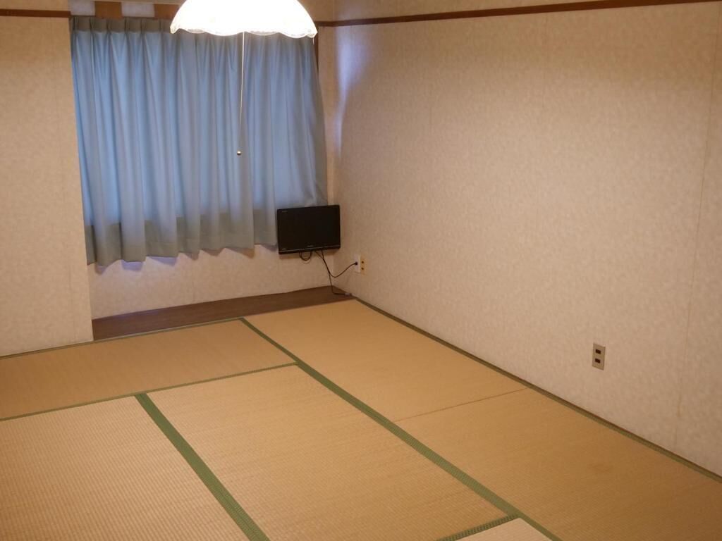 A room with tatami flooring, a television mounted on the wall, and a window with curtains.