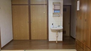Una habitación con un armario de madera, un lavabo blanco y un futón de tatami.