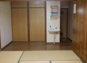 Une pièce avec une armoire en bois, un lavabo blanc et un tatami.