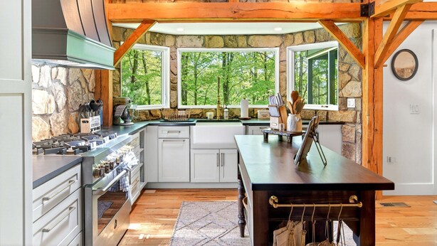 A kitchen with stone walls, wooden beams, and large windows overlooking a forest. - Great Aspen Getaway | Luxury, Pet-Friendly Home with Game Room & Fire Pit! (Black Mountain)