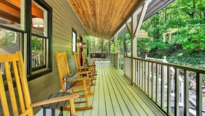 A wooden porch with rocking chairs and a bench, overlooking a forested area. - Great Aspen Getaway | Luxury, Pet-Friendly Home with Game Room & Fire Pit! (Black Mountain)