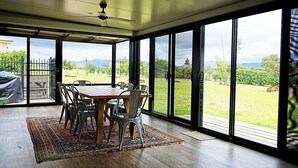 Comedor con una mesa y sillas, puertas de vidrio correderas que dan a un jardín y un ventilador de techo.