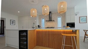 Una cocina moderna con una isla central, luces colgantes y un refrigerador de vinos empotrado.