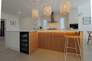 A modern kitchen with a central island, pendant lights, and a built-in wine cooler. - Jasmine Beachside | 60 Secs to Beach, Heated Pool, Whale Season & Fraser Island (Scarness)