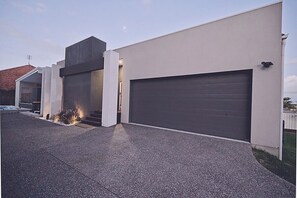 Une maison moderne à deux étages, dotée d’un grand garage, d’une allée couverte et d’un petit foyer extérieur.