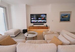 A living room with a flat-screen TV, a sofa, a coffee table, and a painting on the wall. - Jasmine Beachside | 60 Secs to Beach, Heated Pool, Whale Season & Fraser Island (Scarness)