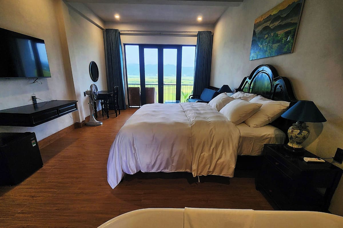 A hotel room with a large bed, a desk, a TV, and a view of the outdoors.