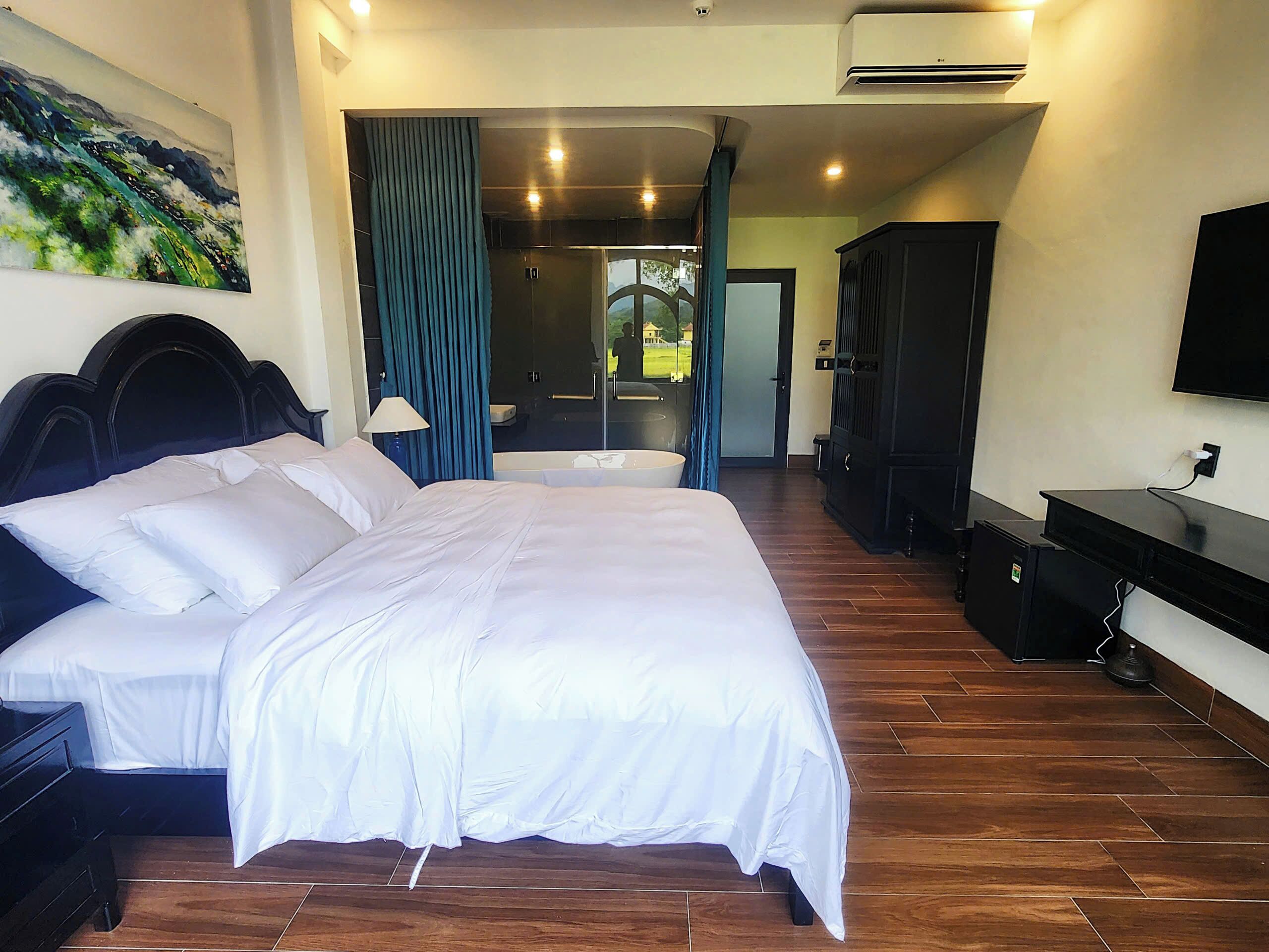 A hotel room with a large bed, a desk, a TV, and a painting on the wall.