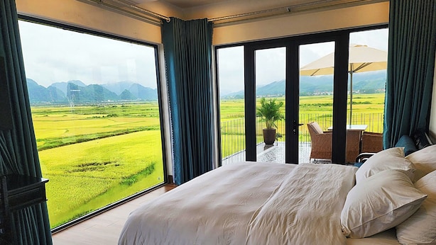 Un dormitorio con una cama grande, vistas a un paisaje verde y un balcón con una silla.