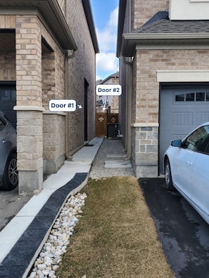 Une rue résidentielle avec deux portes portant les numéros  « Porte n° 1 » et « Porte n° 2 », une allée et des voitures garées.