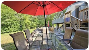 Une table en verre avec des chaises, un parasol rouge et une terrasse en bois dotée d’une rambarde.