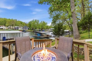 A deck with a fire pit, overlooking a lake with boats and houses. - Lakefront Fun with Private Dock, Firepit, Swim Mat & Screened Patio (Gravois Mills)
