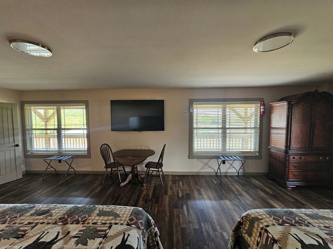 A room with a dining table, two chairs, a TV mounted on the wall, and a wooden cabinet.