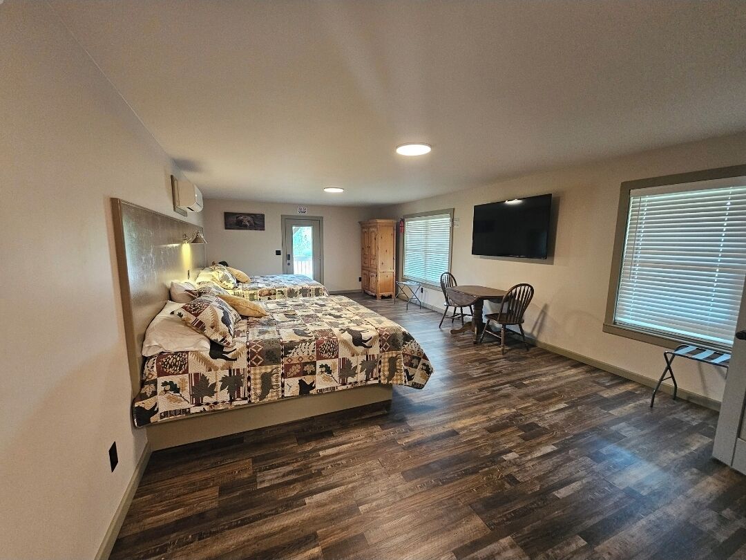 A bedroom with a bed, a desk, a chair, a TV, and a window.