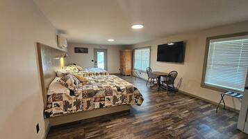 A bedroom with a bed, a desk, a chair, a TV, and a window.