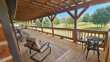 A covered outdoor deck with wooden flooring, metal chairs, and a table.