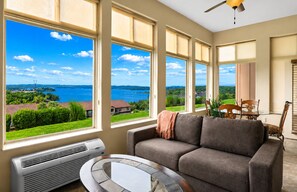 A living room with a large window, a gray sofa, a small table, and a ceiling fan. - Spacious Table Rock Lakeview Condo Near SDC (Branson)