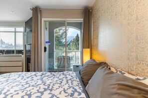Ein Hotelzimmer mit Bett, Fernseher, Balkon mit Blick auf Bäume und Berge sowie einer Schiebetür.