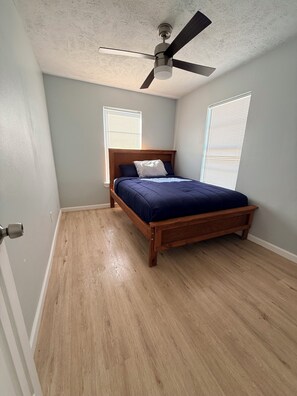 A bedroom with a wooden bed, a ceiling fan, and two windows with blinds. - Enjoyable 2-bedroom house on the intercoastal in charming Sargent, TX (Bay City)