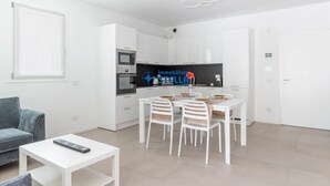 Una cucina moderna con mobili bianchi, un tavolo da pranzo con sedie, un divano grigio e un tavolino da caffè bianco.