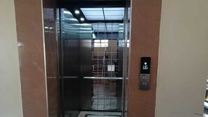An elevator with a control panel, a tiled floor, and a metal door. - A beautiful 2-bedroom unit offering comfort, style, & convenience (Nairobi)