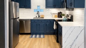 Een moderne keuken met donkerblauwe kastjes, een roestvrijstalen koelkast, een witte marmeren aanrechtblad en een houten vloer.