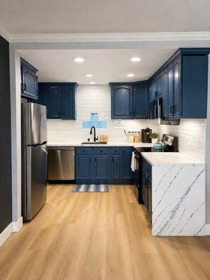 A modern kitchen with dark blue cabinets, a stainless steel refrigerator, a white marble countertop, and a wooden floor. - Stunning Views Beautiful Lakehouse (Discovery Bay)