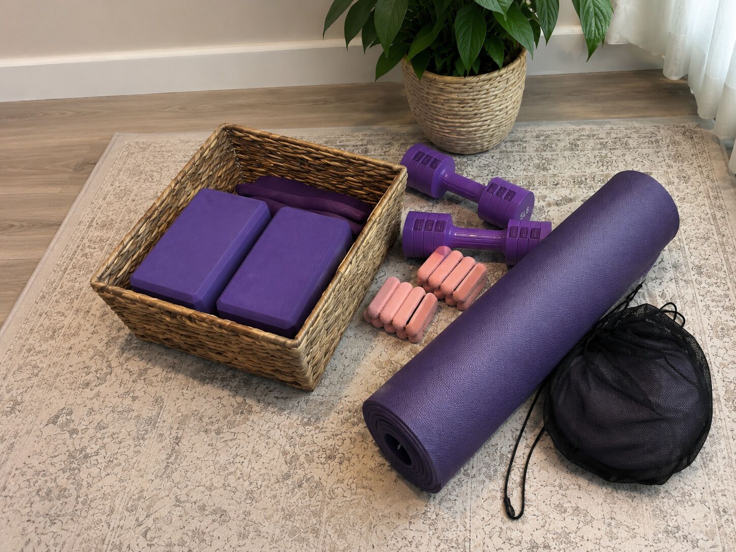 A wicker basket with purple foam blocks, a yoga mat, pink foam blocks, purple dumbbells, and a black mesh bag on a patterned rug.