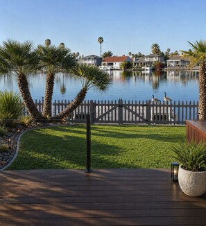 A waterfront property with a wooden deck, a white picket fence, and a calm lake reflecting the houses. - Stunning Views Beautiful Lakehouse (Discovery Bay)