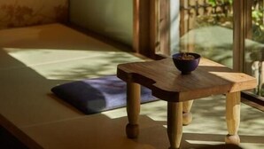 A room with a tatami mat seating area, a small wooden table with a bowl, and a bamboo screen.