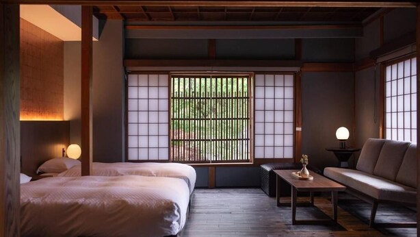 A traditional Japanese-style room with tatami flooring, a low table, a sofa, and a bed with a shoji screen window.