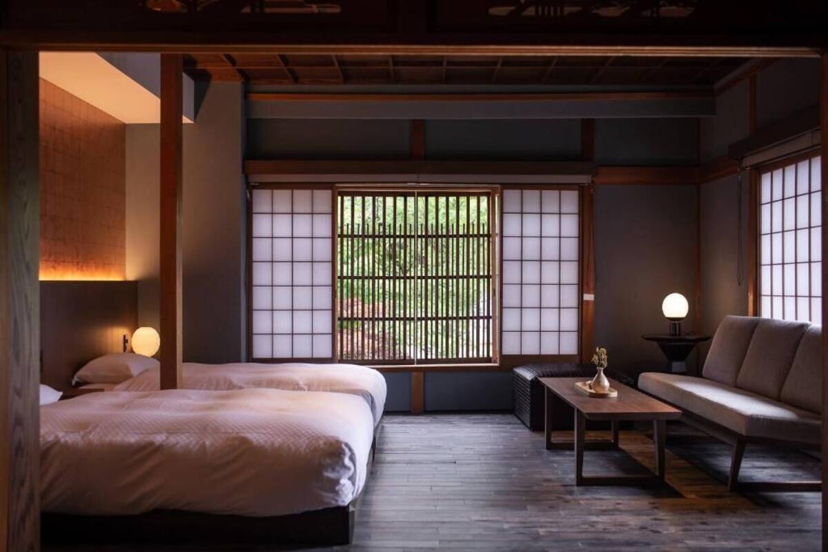 Una tradizionale stanza in stile giapponese, con pavimento in tatami, un tavolino basso, un divano e un letto con finestra a schermo shoji.