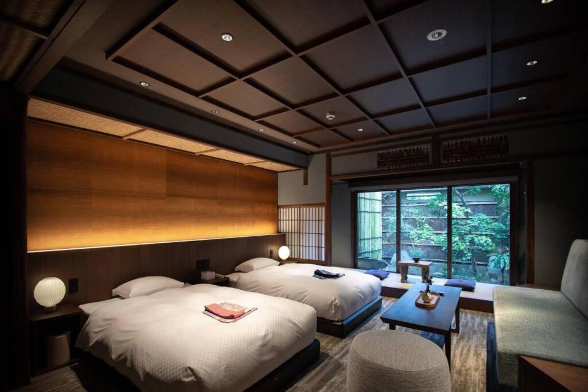 Camera d'albergo con due letti, una zona salotto con tavolo e sedie, un'ampia finestra con vista e un design del soffitto tradizionale.