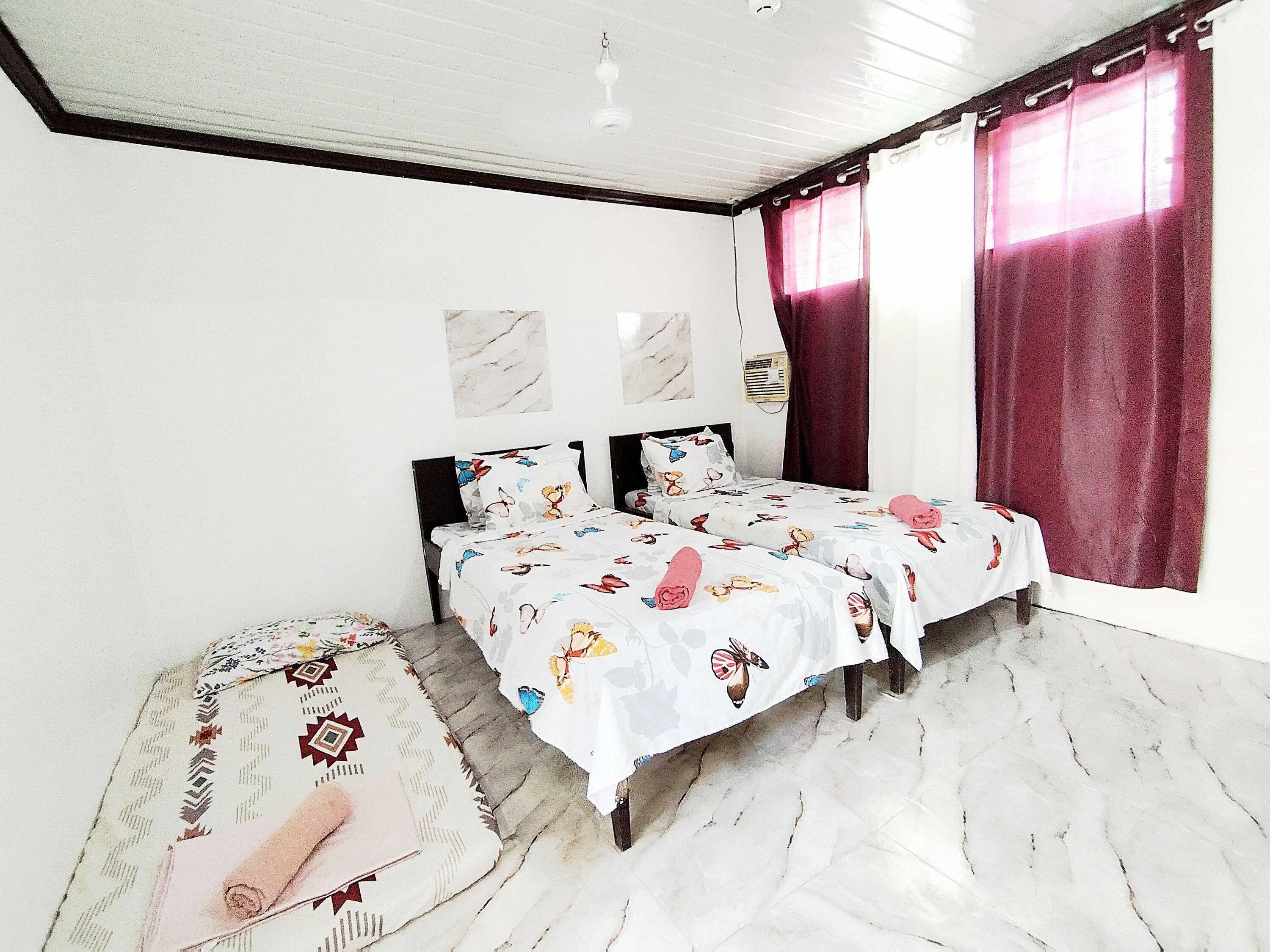 Un dormitorio con dos camas, piso de mármol, ventilador de techo y una ventana con cortinas.