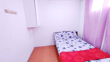 Una habitación pequeña con cama individual, suelo de baldosas, un armario blanco y una ventana con cortinas rosas.