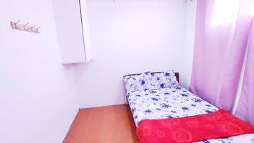 A small room with a bed, a wall-mounted air conditioner, a tiled floor, and a window with curtains.
