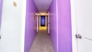 A narrow hallway with purple walls and a carpeted floor, leading to a door with a sign indicating an exit. - OYO 1214 Cherry Travellers Inn (San Jose de Buenavista)