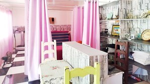A room with a bed, a desk, a chair, a fan, and a shelf with various items. - OYO 1214 Cherry Travellers Inn (San Jose de Buenavista)