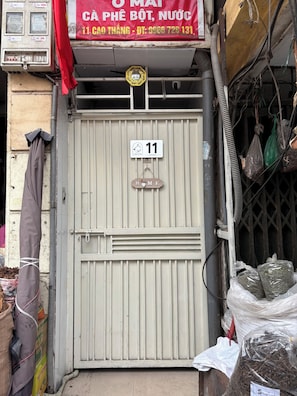 A building with a gated entrance, a sign indicating room number 11, and various items like bags and cables outside. - Private saving room for a solo traveller in Hanoi (Hà Nội)