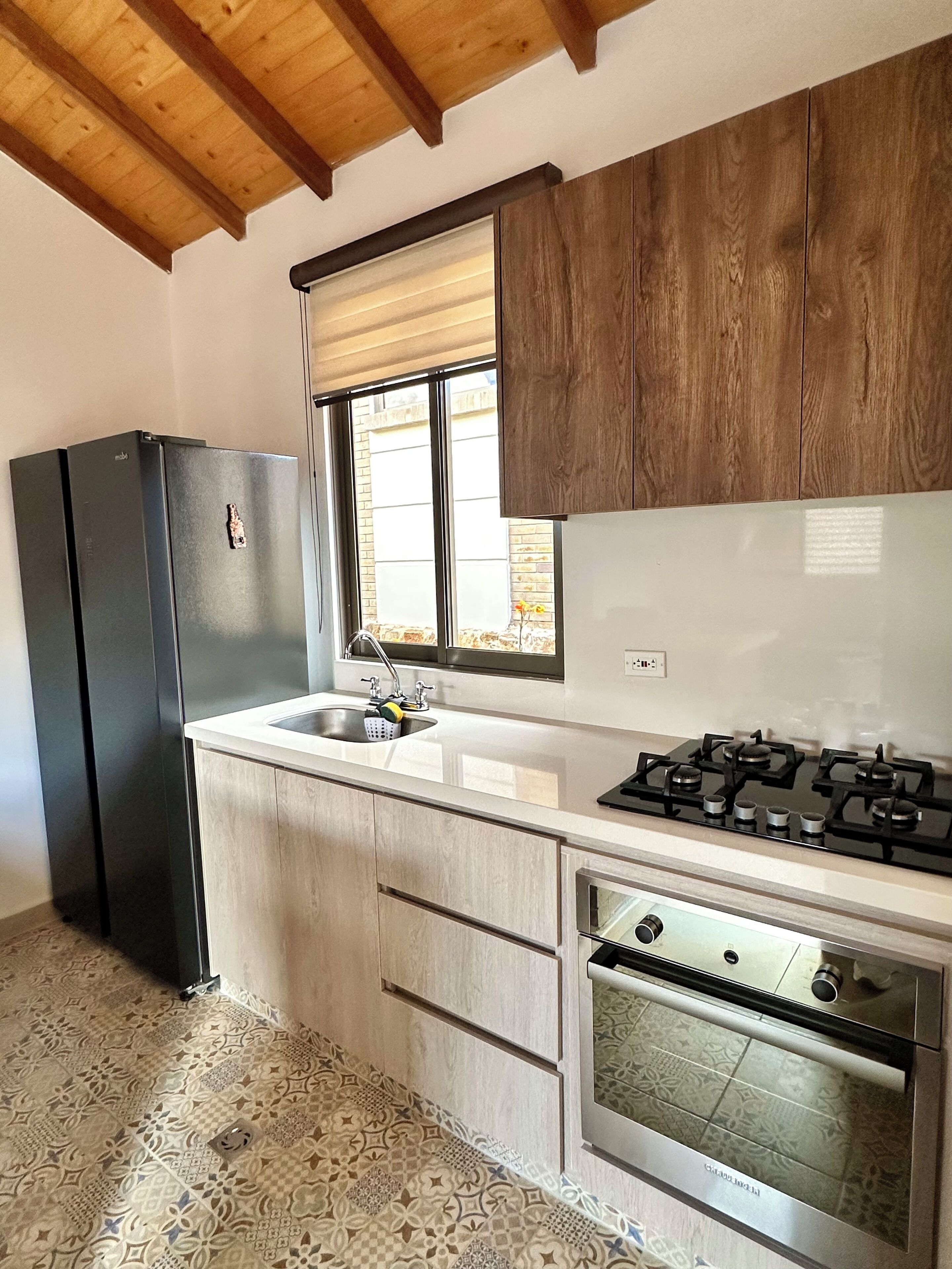 Una cocina con refrigerador, pileta, estufa, horno y alacenas de madera.